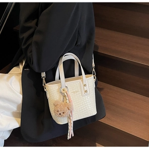 Close-up of white woven bucket bag with gold logo, plush bear charm and tassel detail