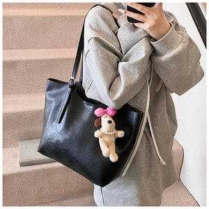 Detail of black tote bag with plush puppy charm and metallic buckle on shoulder strap