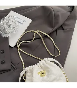Détail du sac seau blanc matelassé avec logo doré et bandoulière chaîne sur un blazer