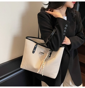 Detail of minimalist beige tote bag with black trim and elegant tassel on model