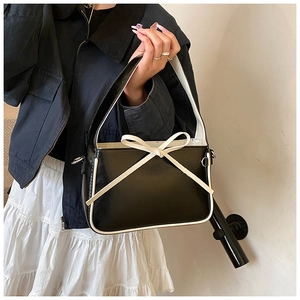 Détail d'un sac seau en cuir verni noir avec passepoil blanc et un nœud décoratif