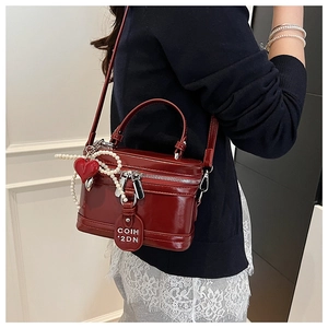 Detail of glossy red vintage box bag with heart pearl charm and elegant top handle
