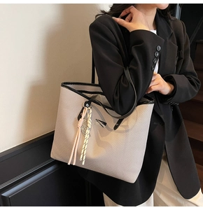 Detailed shoulder view of large gray woven tote bag with black leather trim and tassel