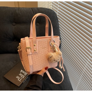 Detailed view of pink woven bucket bag with golden buckle and brown teddy bear charm