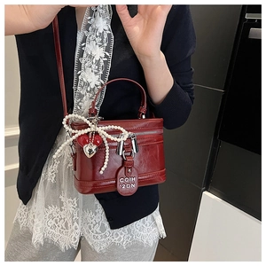 Detail of dark red vintage box bag with pearl bow and heart charms on a model