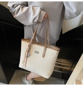 Detail of beige woven tote bag featuring brown faux leather straps and a decorative tassel