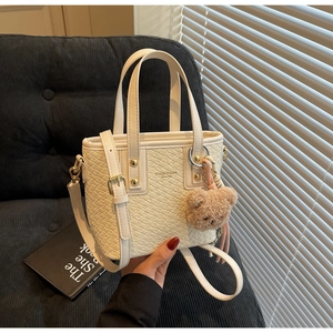 Detail of cream woven bucket bag with gold hardware and plush bear charm accent