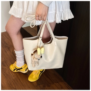 Detail of off-white tote bag featuring silver buckles and a cute plush puppy charm