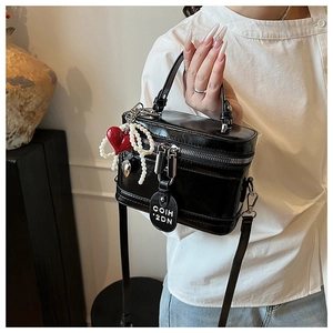 Detail of black glossy box bag with red heart and pearl charms on white shirt background