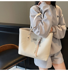 Detail view of beige tote bag with twill texture and decorative metal hardware tassel