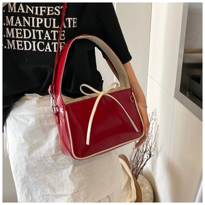 Détail du sac seau en cuir verni rouge avec nœud blanc contrasté et bandoulière fine