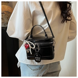 Detail of a black glossy leather box bag featuring a pearl chain and heart charms decoration