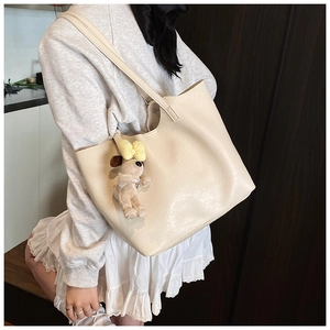 Detail of cream white tote bag with natural leather texture and cute puppy charm on shoulder