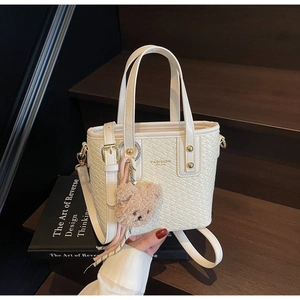 Detail of cream woven bucket bag with gold lettering and cute plush bear charm