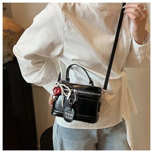 Detail of black glossy box bag featuring pearl bow and red heart charms on model