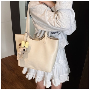 Detail of off-white tote bag with litchi texture and cute plush dog pendant charm