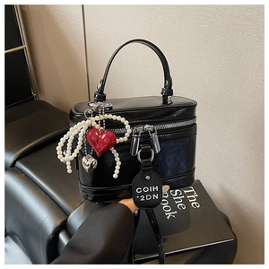 Detail of black glossy box bag with pearl strand, red heart charm, and silver heart pendant