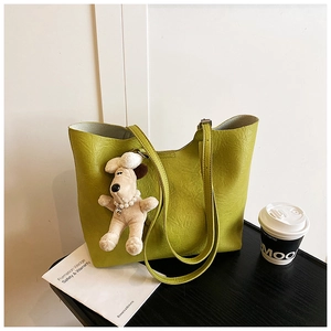 Detail of avocado green tote bag with lychee texture and cute plush dog charm on desk