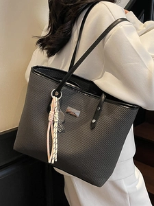 Minimalist black woven tote bag with shoulder straps and decorative colorful tassel