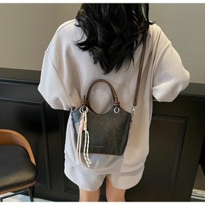 Détail d'un sac seau noir mat avec poignées rondes marron et pendentif à nœud décoratif