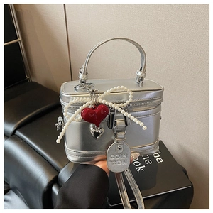 Detail view of silver metallic box bag with pearl bow and red heart charm accent
