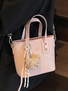 Pink woven texture bucket bag with bear pendant shown on model in a stylish setting