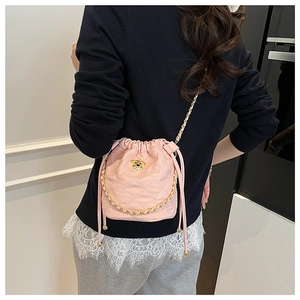 Détail du sac seau rose matelassé avec ours doré et bandoulière chaîne sur un modèle