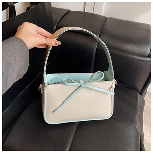 Gros plan d'un sac seau crème avec nœud en cuir bleu clair et détails de boucle en métal