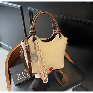 Détail du sac seau beige avec bord ondulé, poignée marron foncé et pendentif tennis argenté