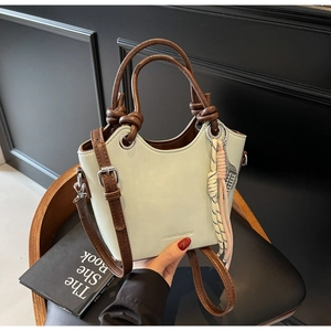 Détail du sac seau vert clair avec poignée tressée marron et accessoire rayé suspendu