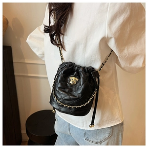 Détail d'un sac seau matelassé noir avec chaîne dorée et logo porté par un mannequin