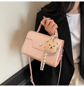 Detail of pink faux leather crossbody bag with teddy bear charm and round buckle