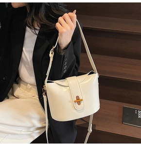 Detail of a creamy white bucket bag with a golden turn-lock closure and adjustable strap