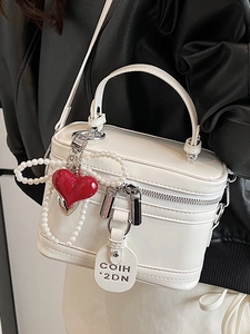 White patent leather box bag with pearl bow and heart charm worn as a crossbody