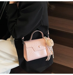 Detail of pink pleated crossbody bag with plush bear charm worn on dark wood steps