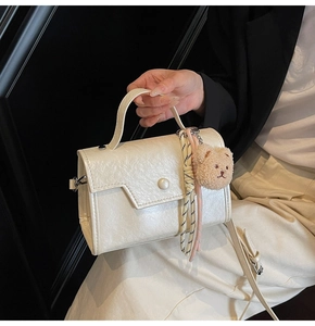 Detail of cream leather square bag with pearl buckle, plush bear, and woven strap detail