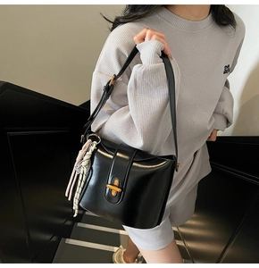 Detail of black faux leather crossbody bag featuring a golden twist lock and tassel