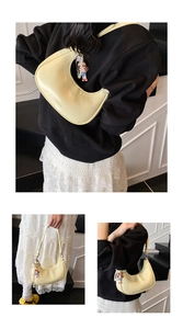 Detail of yellow crescent shoulder bag with polished finish and a pearl doll charm