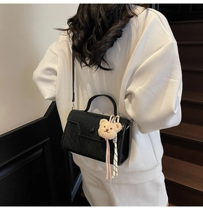 Detailed back view of a black crocodile-pattern handbag with a cute plush bear charm