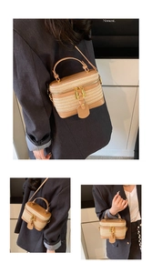 Detail view of woven straw box bag with brown leather trim and golden metal zippers