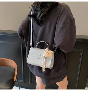 Close-up of a silver crossbody bag with a bear charm on a model in a minimal setting