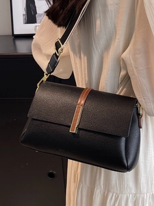 Minimalist black pebble leather crossbody bag with wide strap on a model wearing white dress