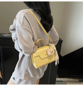 Detail of yellow rectangular crossbody bag featuring round buckle and bear charm