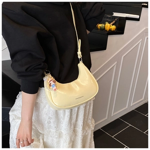 Détail d'un sac demi-lune jaune crème avec finition brillante et breloque en perles