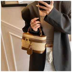 Detail view of woven straw box bag with brown leather trim and golden metal zippers