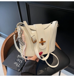 Detail of white bucket bag with gold lock, pink braided tassel and adjustable strap