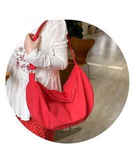 Detail view of a large red crescent crossbody tote bag with a wide nylon shoulder strap