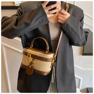 Detail of woven straw box bag with brown leather trim and gold zippers on model