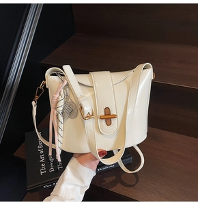 Close-up of beige leather handbag featuring a gold buckle lock and decorative charms