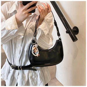 Close-up of black glossy leather hobo bag with a cute pearl charm and fashion logo